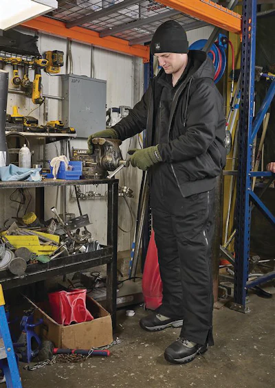 Worker in black winter gear using industrial tools in warehouse workshop