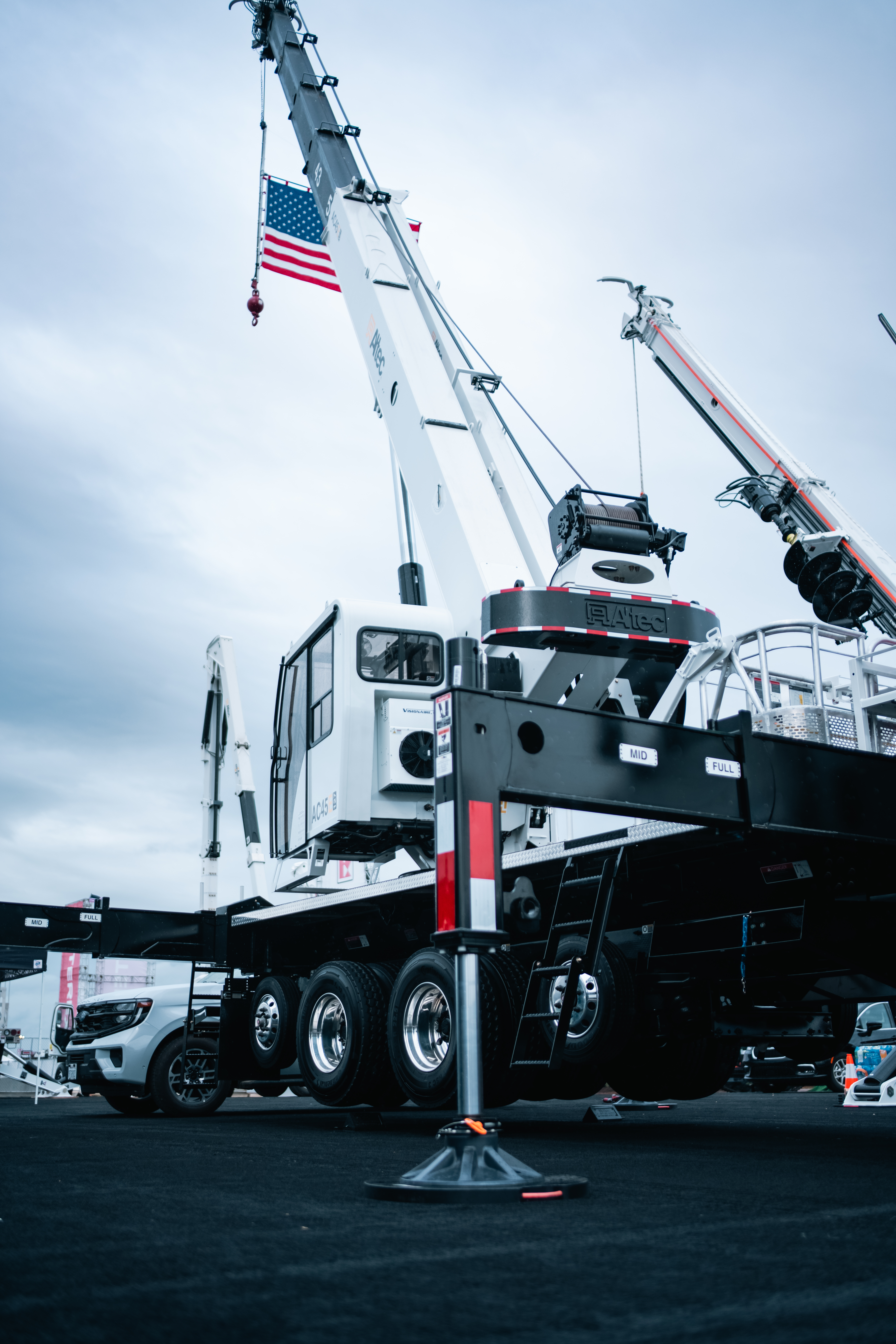 White mobile crane with extended boom and American flag on industrial site