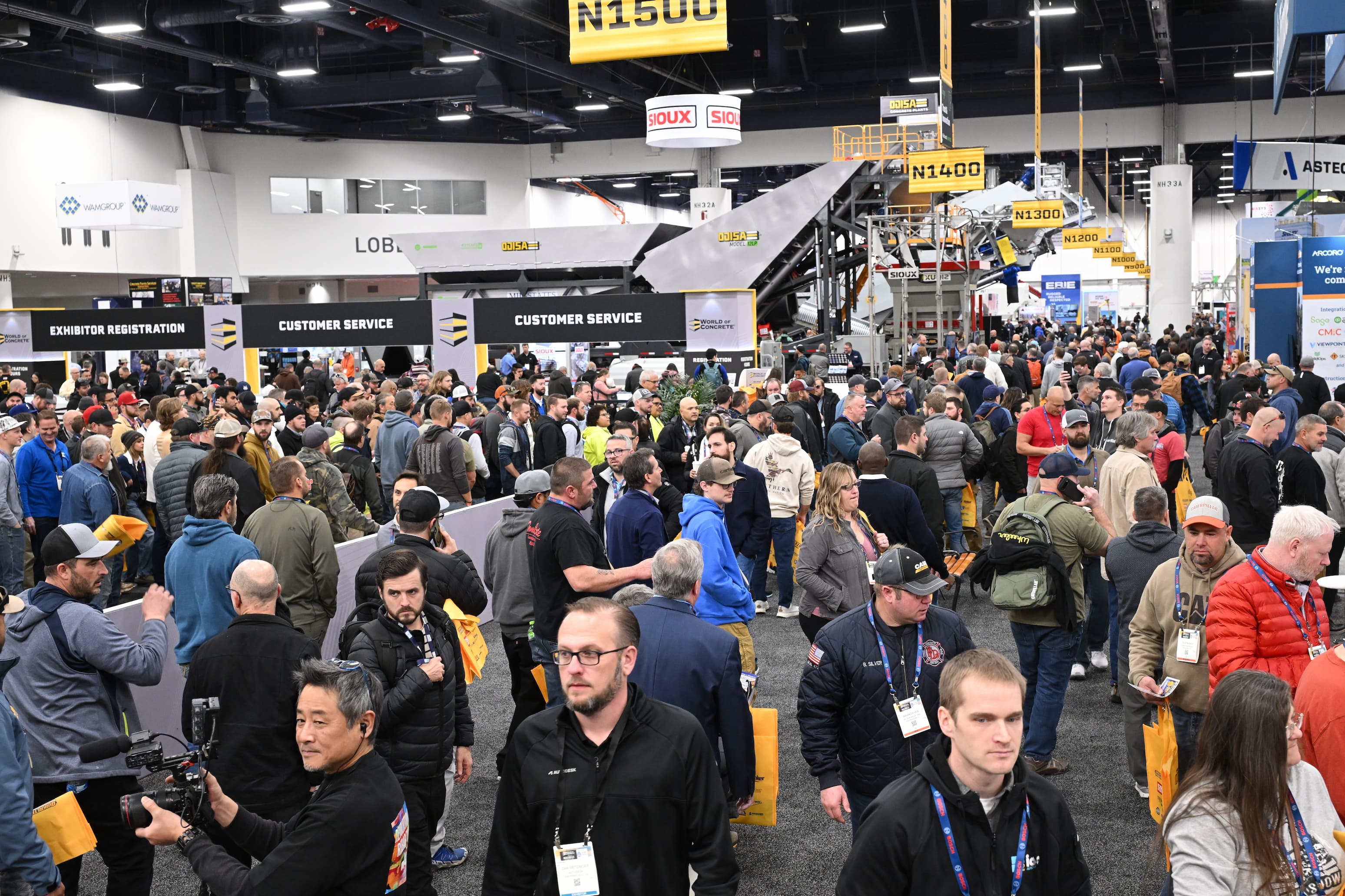 Crowded industrial trade show with attendees walking between customer service and registration areas
