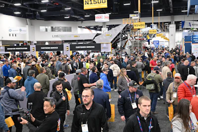 Crowded industrial trade show with attendees walking between customer service and registration areas