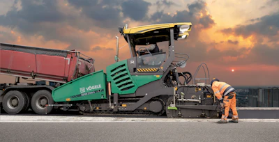 Road paving machine at sunset with worker preparing asphalt surface