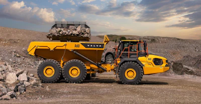Yellow Volvo articulated dump truck loaded with rocks in rocky quarry landscape