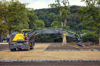 Yellow Volvo wheeled excavator preparing ground at construction site with trees
