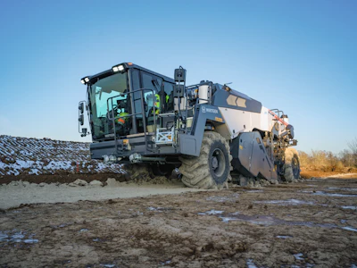 Heavy construction vehicle operating on muddy terrain with snow patches