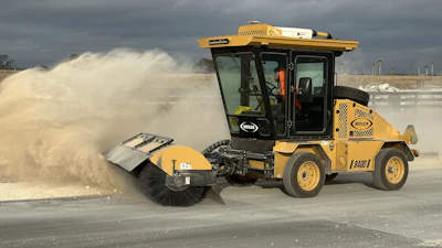 Yellow road sweeper machine clearing dust on construction site with cloudy sky