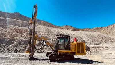 Yellow tracked drilling rig operating in rocky desert mining terrain