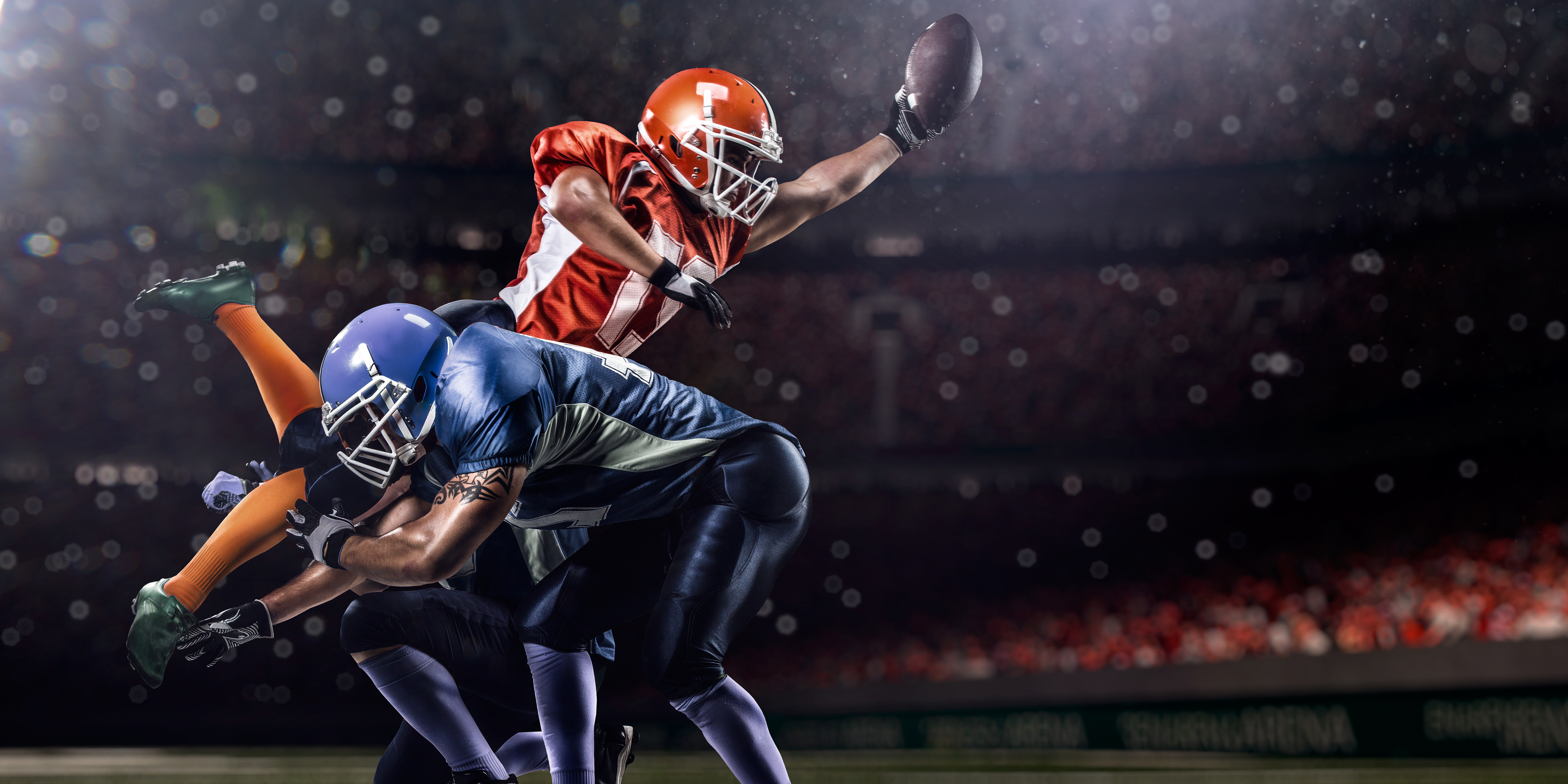 Football players in mid-action, one leaping to catch ball while another defends