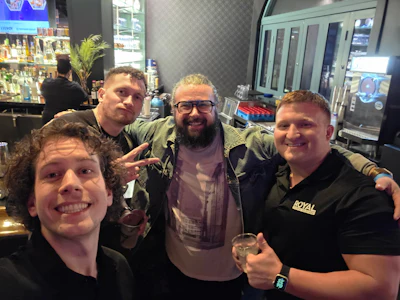Four friends smiling together at a bar with drinks and a Royal logo shirt
