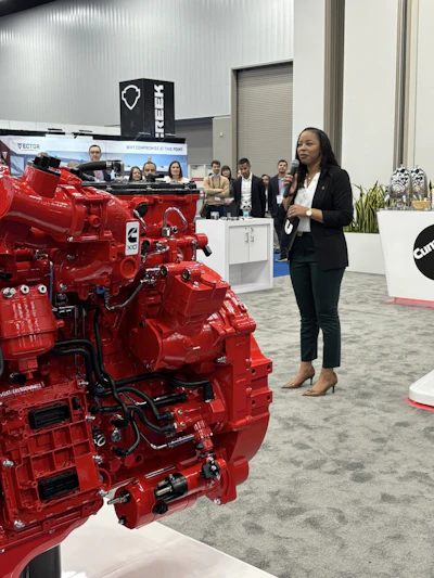 Woman presenting a bright red Cummins diesel engine at an industrial trade show exhibition with attendees in background