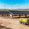 Renewable energy facility with solar panels, wind turbines, and yellow portable generator equipment on sandy terrain