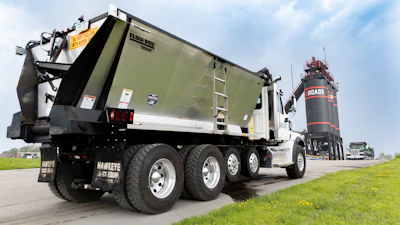 White and olive green commercial dump truck with Hawkeye Gold Group branding on highway with grain silo in background