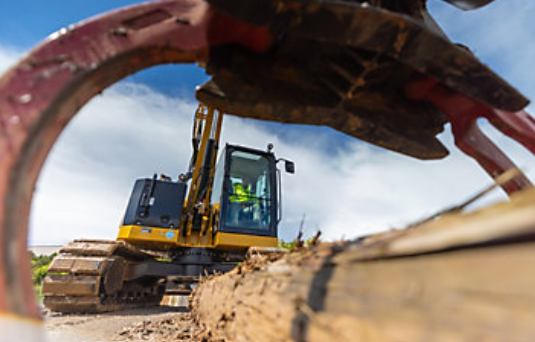 Yellow excavator working on dirt terrain with construction equipment in background