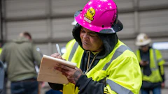 Construction worker in bright safety vest and pink hard hat taking notes on clipboard