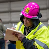 Construction worker in bright safety vest and pink hard hat taking notes on clipboard