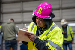 Construction worker in bright safety vest and pink hard hat taking notes on clipboard