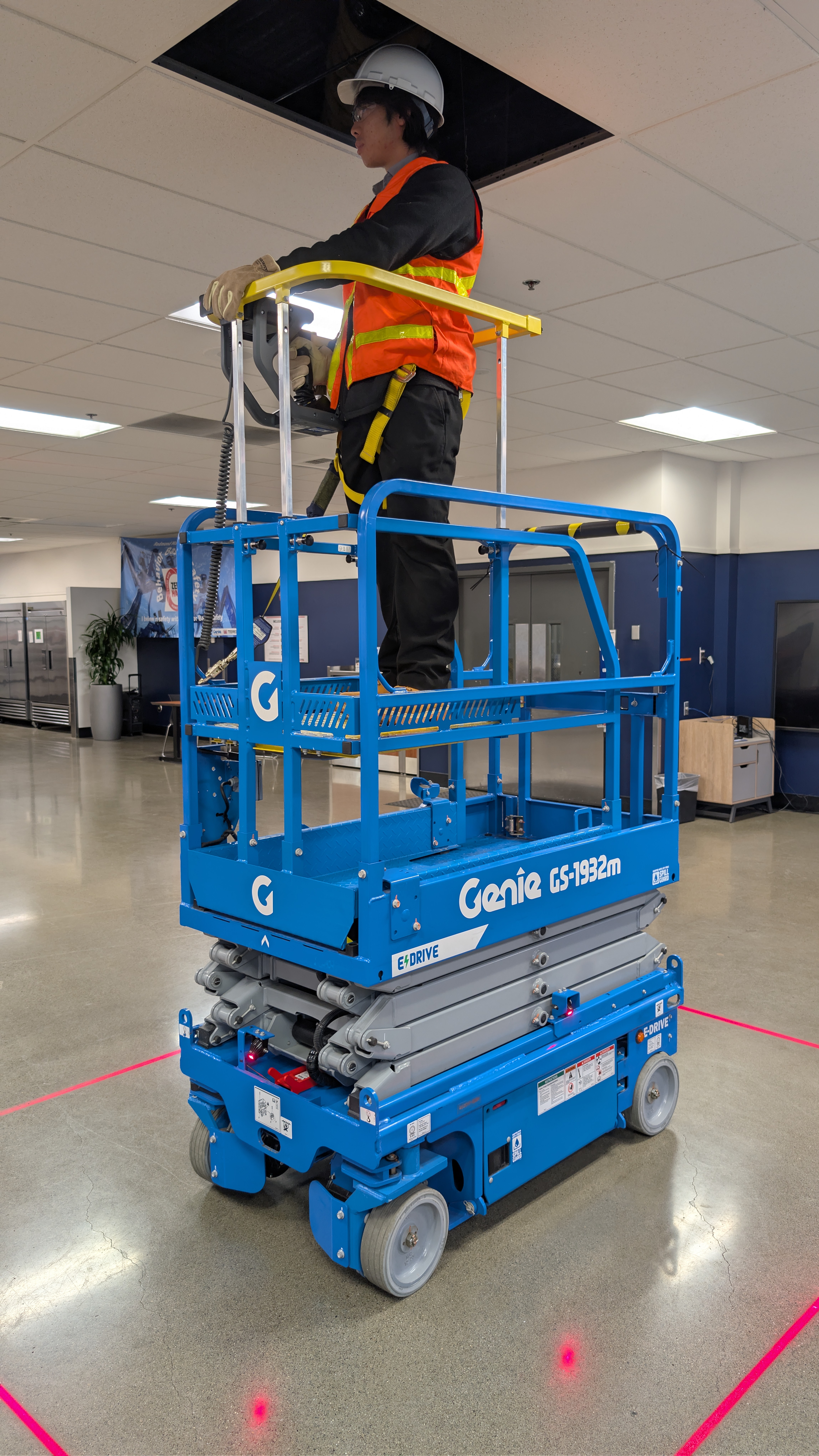 Blue Genie scissor lift with worker in safety vest and hard hat inside industrial facility