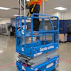Blue Genie scissor lift with worker in safety vest and hard hat inside industrial facility