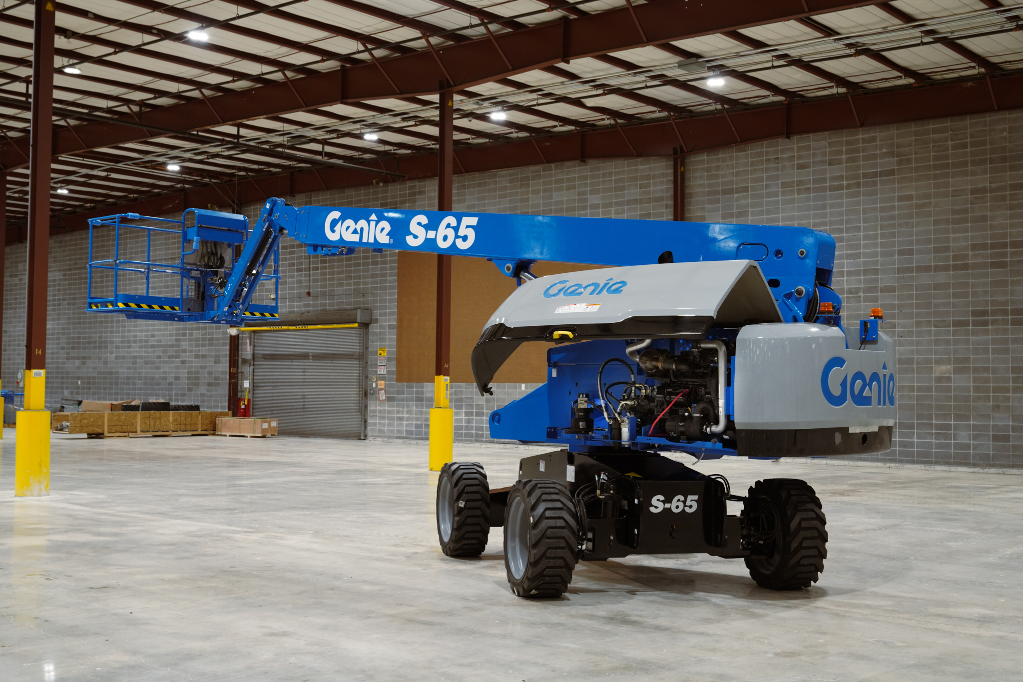 Blue Genie S-65 boom lift positioned in an industrial warehouse with concrete flooring and brick walls