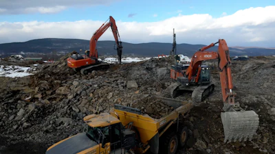 Orange excavators and yellow dump truck working on rocky construction site with mountains