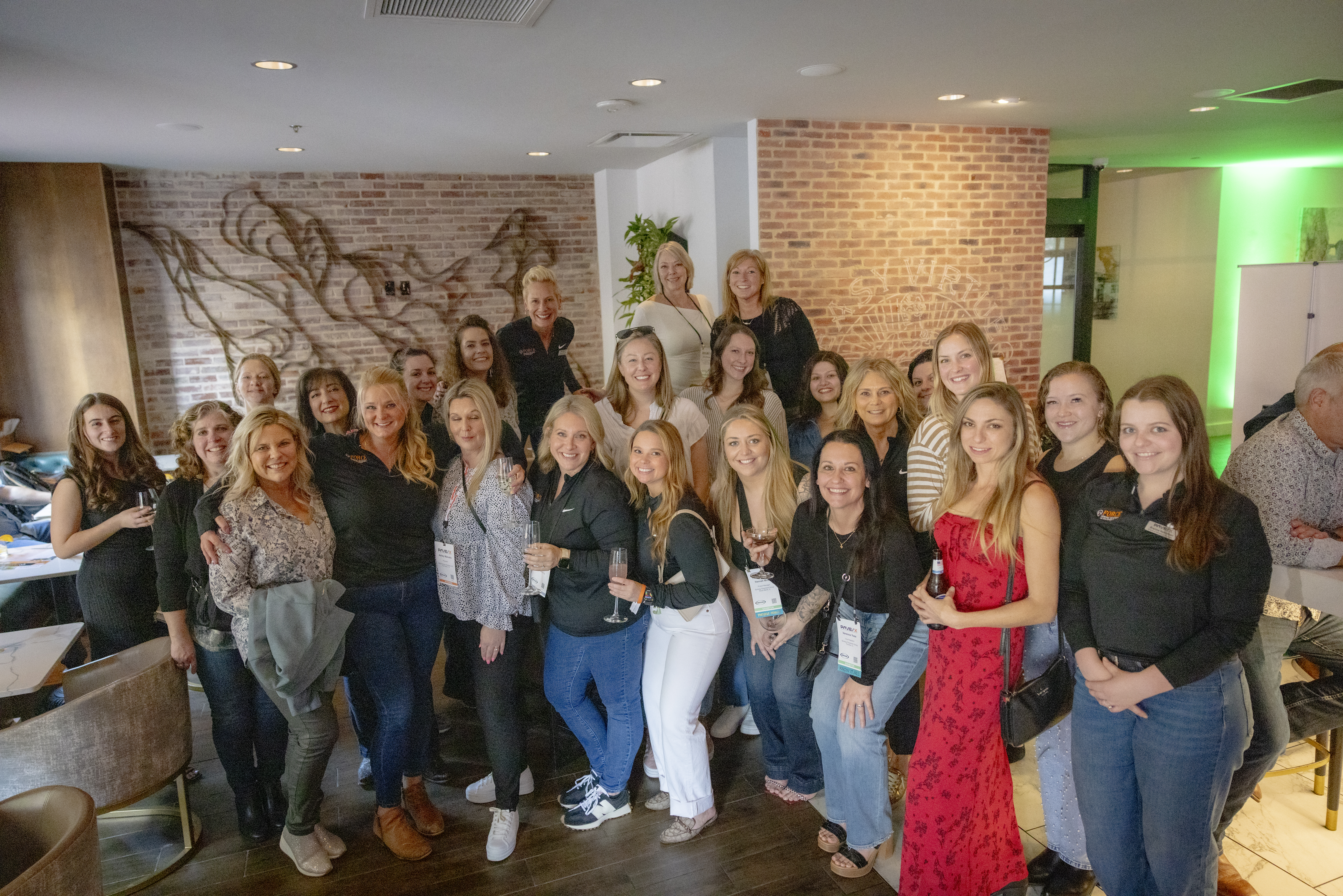 Large group of professional women posing together at indoor corporate event with brick walls
