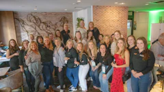 Large group of professional women posing together at indoor corporate event with brick walls