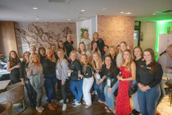 Large group of professional women posing together at indoor corporate event with brick walls