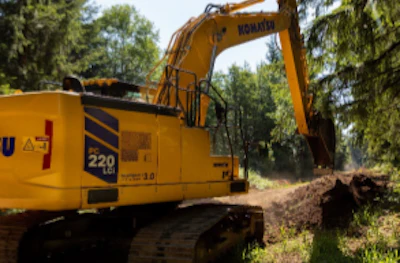 Yellow Caterpillar excavator operating at a construction site surrounded by trees and wood debris