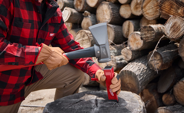 Person in red plaid shirt splitting wood with an axe in front of stacked logs