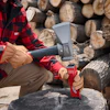 Person in red plaid shirt splitting wood with an axe in front of stacked logs