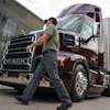 Professional truck driver walking beside maroon Mack semi-truck in urban loading area