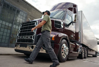 Professional truck driver walking beside maroon Mack semi-truck in urban loading area
