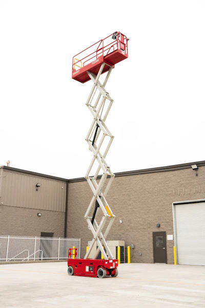 Red and white scissor lift platform extended to full height outside an industrial building