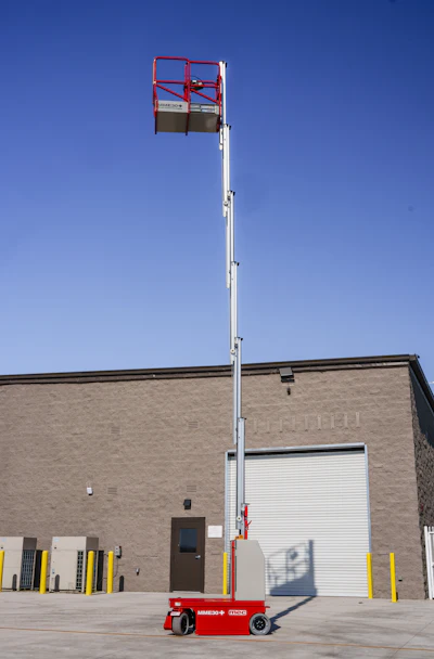 Red and white aerial lift platform extended against clear blue sky in front of brick industrial building