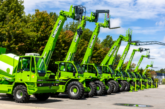 Green Merlo telehandlers lined up in a row with trees and blue sky background