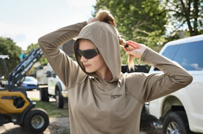 Person in beige Milwaukee hoodie adjusting hood, standing near work vehicles