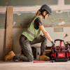 Construction worker in safety vest and helmet kneeling beside red Milwaukee tool bag