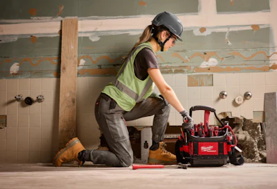 Construction worker in safety vest and helmet kneeling beside red Milwaukee tool bag