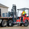 Red forklift loading blue pallets onto flatbed truck at industrial site