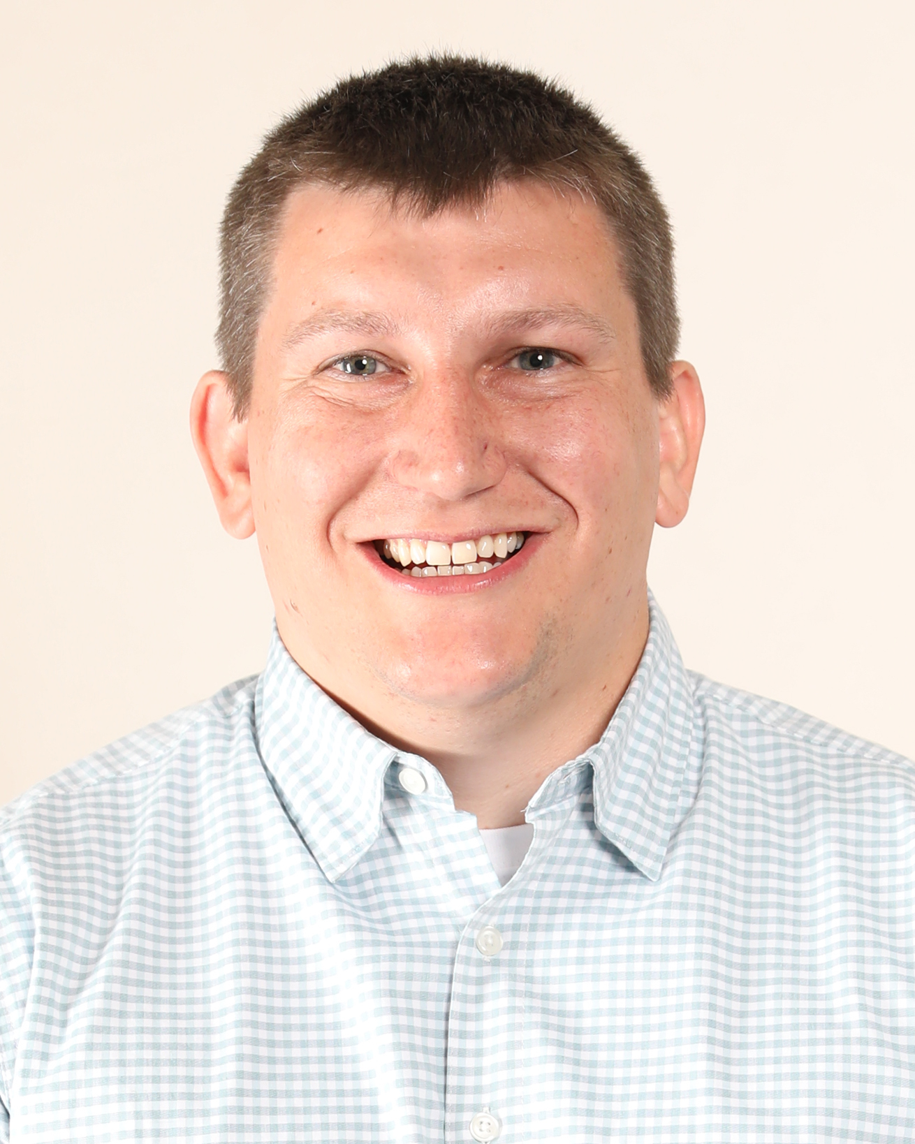 Smiling man in light blue checkered shirt against neutral background Headshot