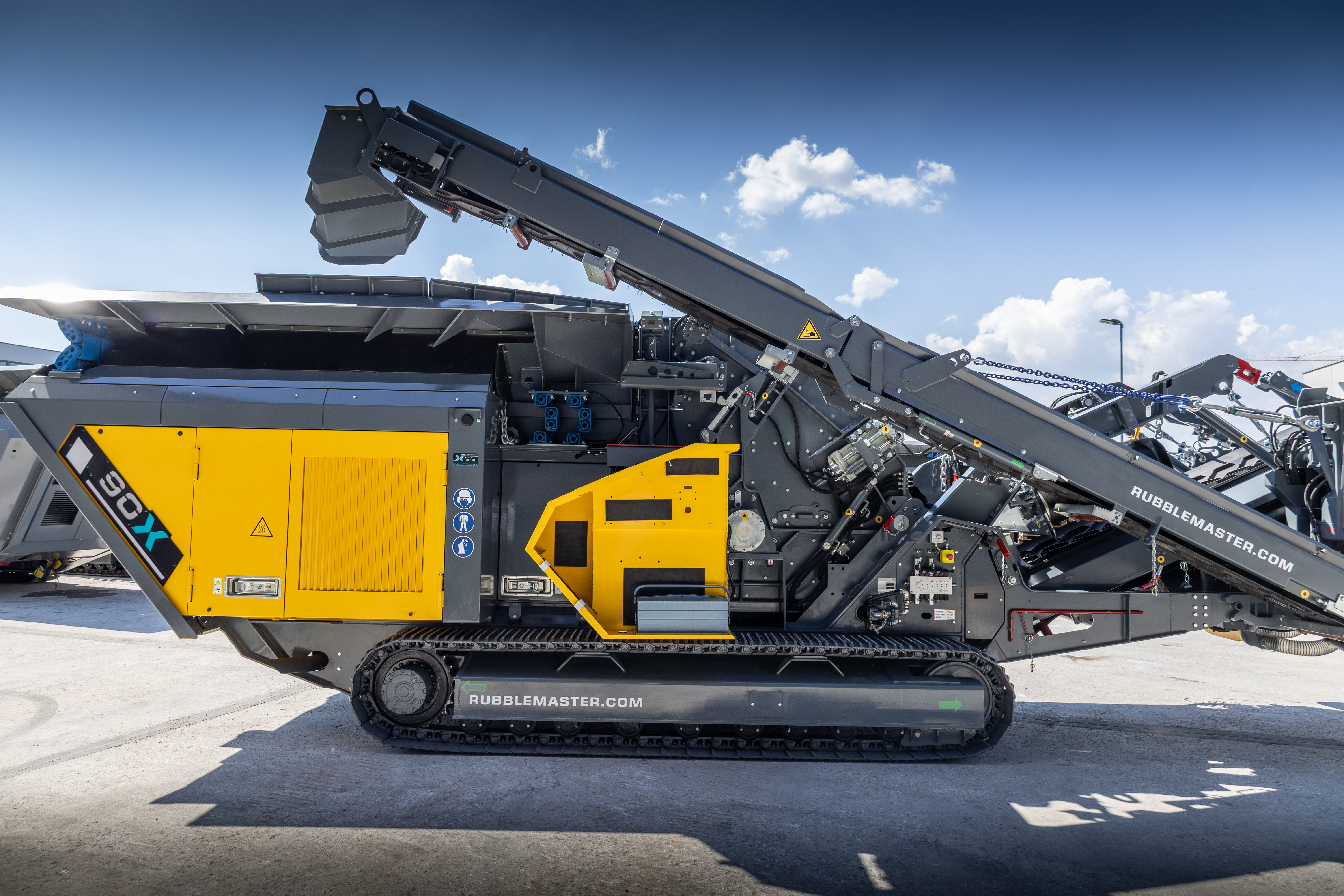 Yellow and gray tracked mobile industrial crusher on concrete with raised conveyor arm