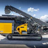 Yellow and gray tracked mobile industrial crusher on concrete with raised conveyor arm