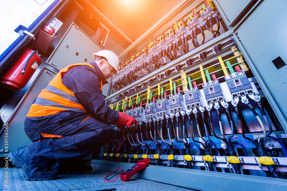 Technician in safety vest inspecting electrical control panel with complex wiring