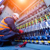 Technician in safety vest inspecting electrical control panel with complex wiring