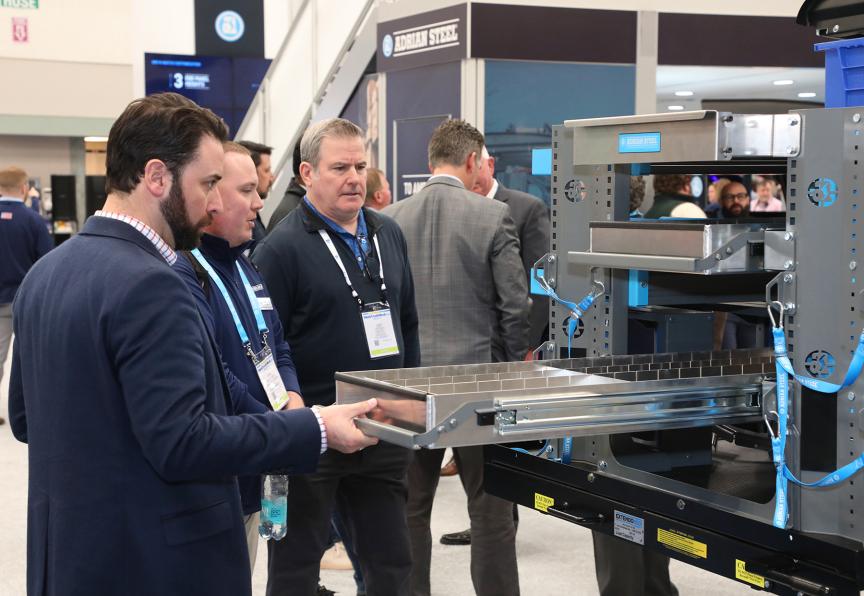 Professionals examine industrial 3D printing equipment at a technology trade show or conference event