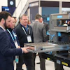 Professionals examine industrial 3D printing equipment at a technology trade show or conference event