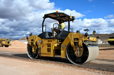 Yellow Caterpillar asphalt roller compactor on construction site with other heavy equipment and blue sky