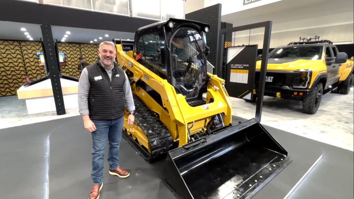 Man standing next to yellow Caterpillar skid steer loader in equipment showroom with additional vehicles displayed