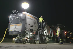 Wirtgen asphalt paver machine operating at night with workers in safety gear and illuminated work lights
