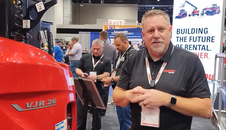 Professionals at trade show examining red VJR 26 equipment with branded signage in background