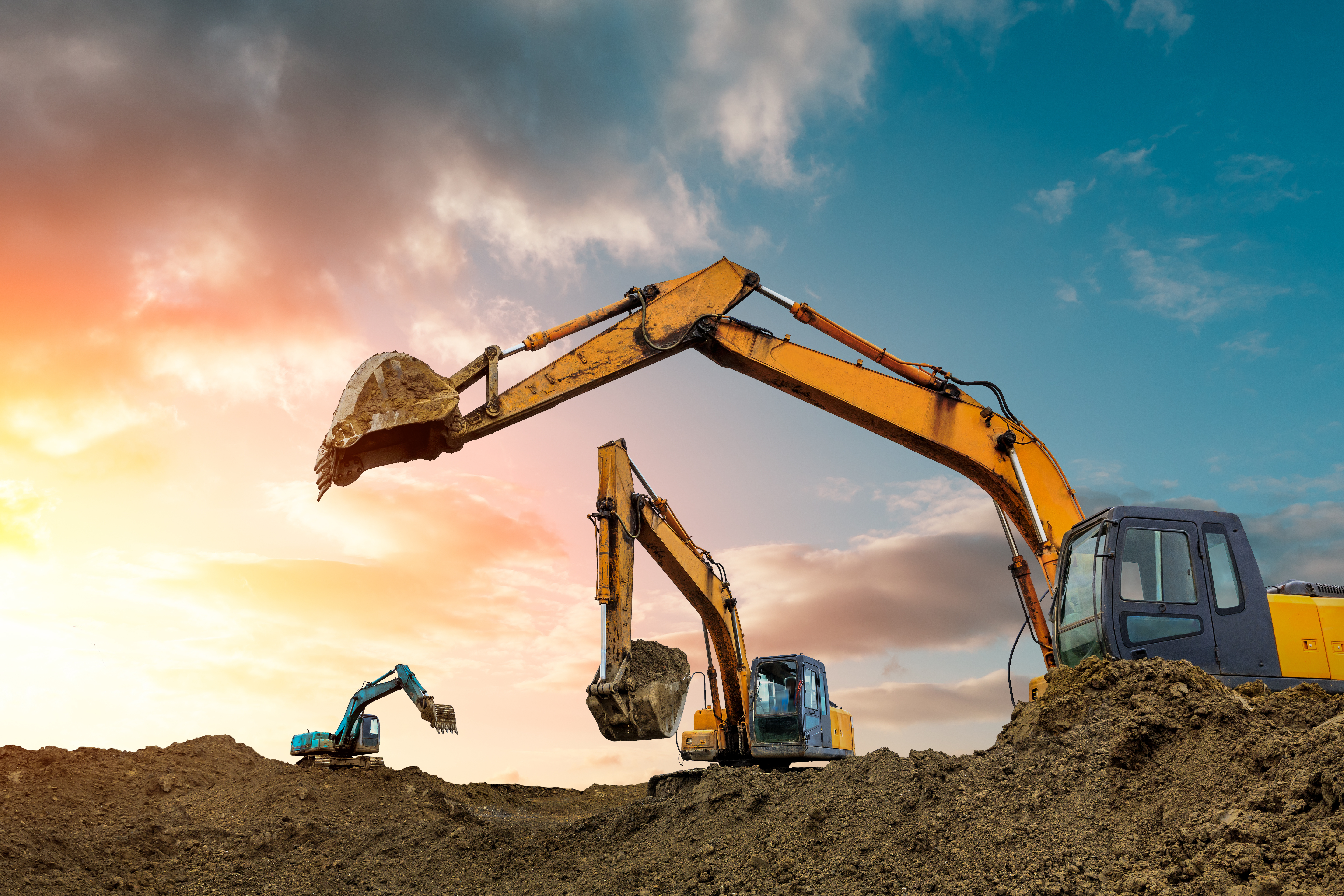 Heavy excavators operating on a construction site during golden hour with dramatic sky and earth mounds